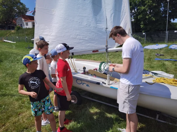 Gruppe von Kindern beobachtet einen jungen Mann beim Segeln der Jolle.